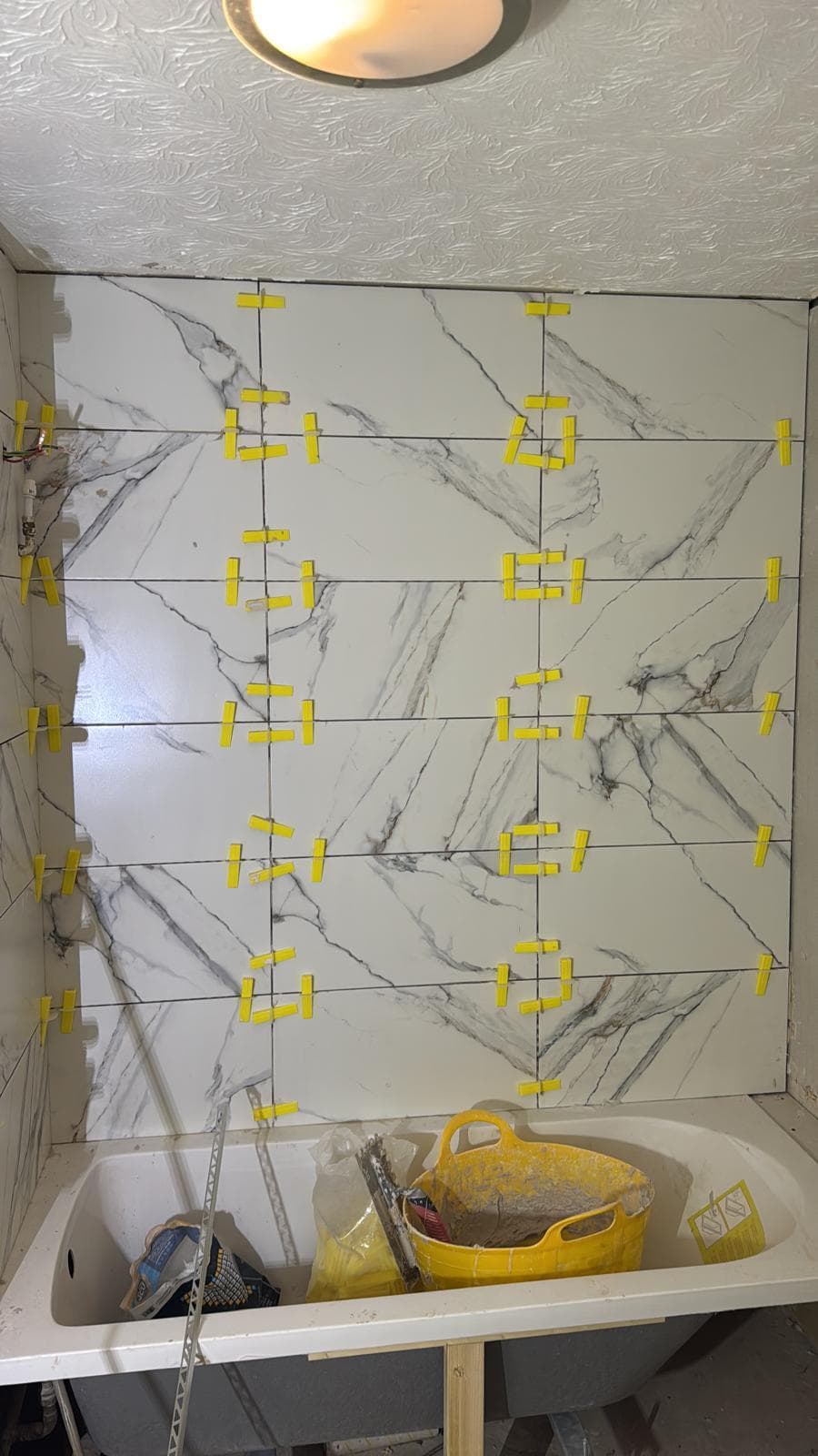Marble Family Bathroom in Hammersmith: Marble going up on levelling clips, veining set out