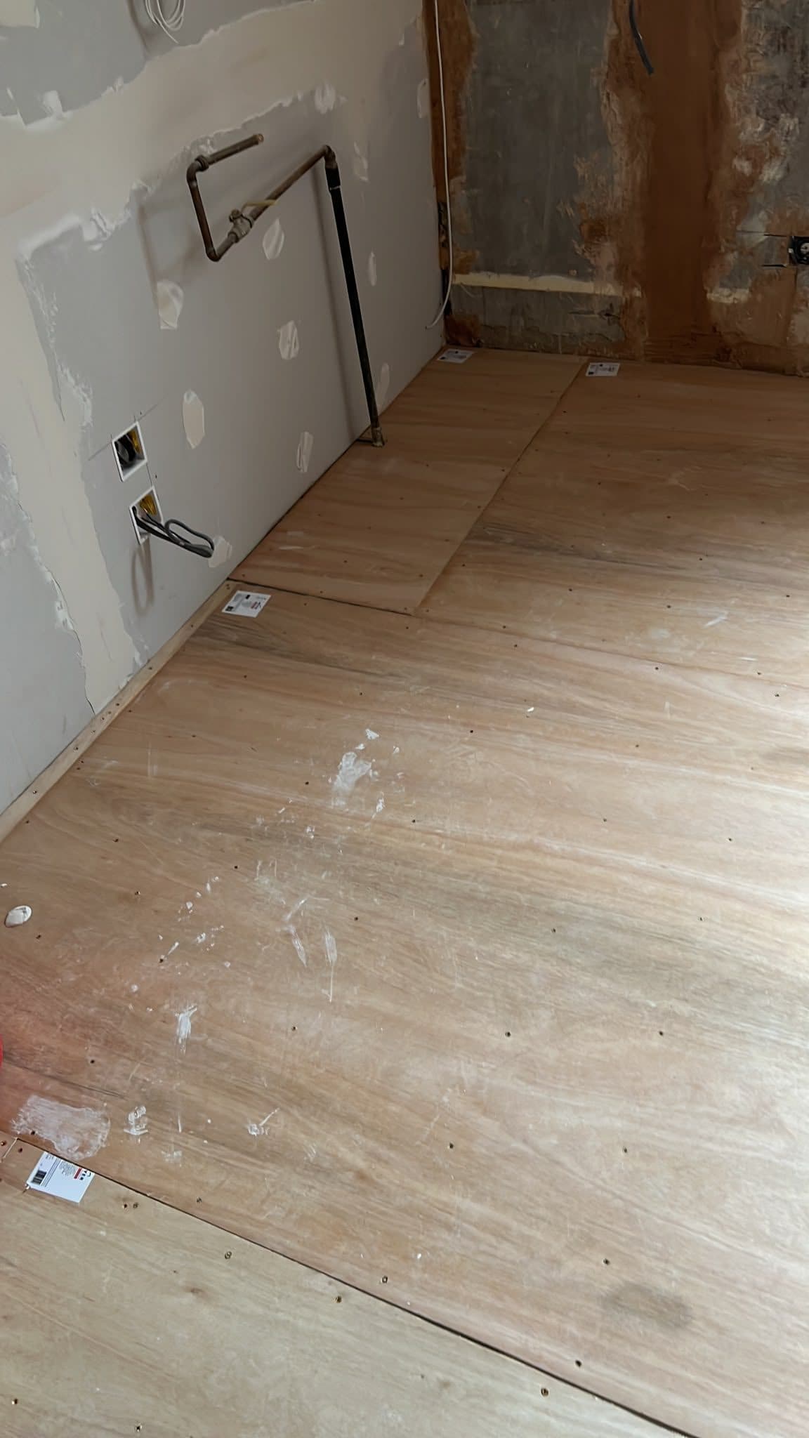Kitchen Renovation in Tooting: New plywood subfloor laid, with supply pipes coming through the wall